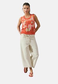 Top de punto floral en naranja y rosa con escote acanalado, combinado con pantalones beigos de corte holgado y chanclas rojas.