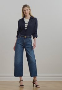 Tumši zili pogājami krekli, balti svītroti topi, augstā jostasvieta plata kāju džinsi un melnas korsetes kurpes. Gluda tekstūra, klasiskā dizaina.