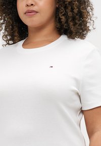 White cotton t-shirt with a crew neckline and short sleeves, featuring a small logo in red, white, and blue on the left chest.