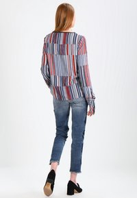 Camicia a righe a maniche lunghe blu, rossa e bianca con una vestibilità comoda; abbinata a jeans sbiaditi e scarpe con tacco nere.