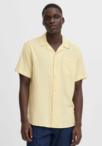 Camicia a maniche corte con colletto di colore giallo chiaro, realizzata in tessuto texturizzato. Presenta una tasca sul petto e bottoni lungo la parte anteriore.
