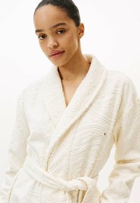 Accappatoio color crema con motivi in rilievo intricati. Presenta un colletto a scialle, cintura e tessuto testurizzato per un effetto più profondo.