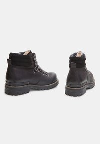 Botas de senderismo de cuero negro con un cuello acolchado, suela de goma y cordones grises; cuentan con ojales reforzados y soporte texturizado en el tobillo.