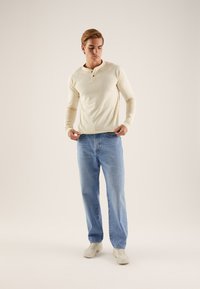 Svetlo bež majica Henley z dolgimi rokavi in gumbi, kombinirana z širokimi svetlo modrimi kavbojkami in bež supergami. Preprost in moderen dizajn.