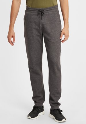 Graue, gestrickte Jogginghose mit elastischem Bund und verstellbarem Kordelzug. Mit Seitentaschen und schmal zulaufenden Beinen. Getragen mit schwarzen Sportschuhen.