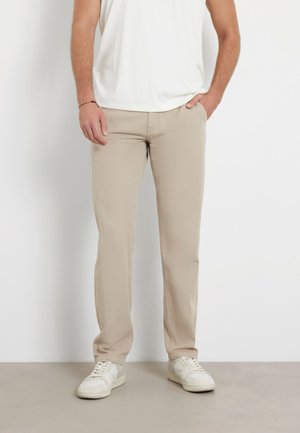 Pantaloni beige a gamba dritta realizzati in cotone con una texture liscia. Abbinati a sneakers bianche e una camicia bianca aderente. Nessun motivo visibile.