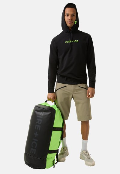 Black hoodie with green "FIRE+ICE" logo, beige shorts, and carrying a green and black duffel bag with branding and handles.
