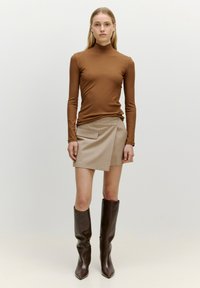 Bruine geribbelde coltrui, beige wikkelrok met zijzak en knielange bruine leren laarzen met puntige neuzen. Gladde textuur, aansluitend ontwerp.