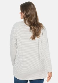 Camicia a maniche lunghe con collo a giro in tessuto morbido, caratterizzata da sottili righe orizzontali beige e marrone scuro. Vestibilità rilassata con spacco laterale.
