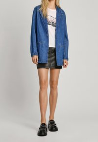 Džínová sako, světle modré, nošené přes bílé tričko s potiskem. Černá kožená mini sukně a lesklé černé platformové boty se cvočky.