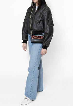 Veste bomber en cuir noir, jeans évasés bleu clair et chaussures blanches avec des éléments en métal argenté. Petit sac noir avec des rayures rouges et bleues.