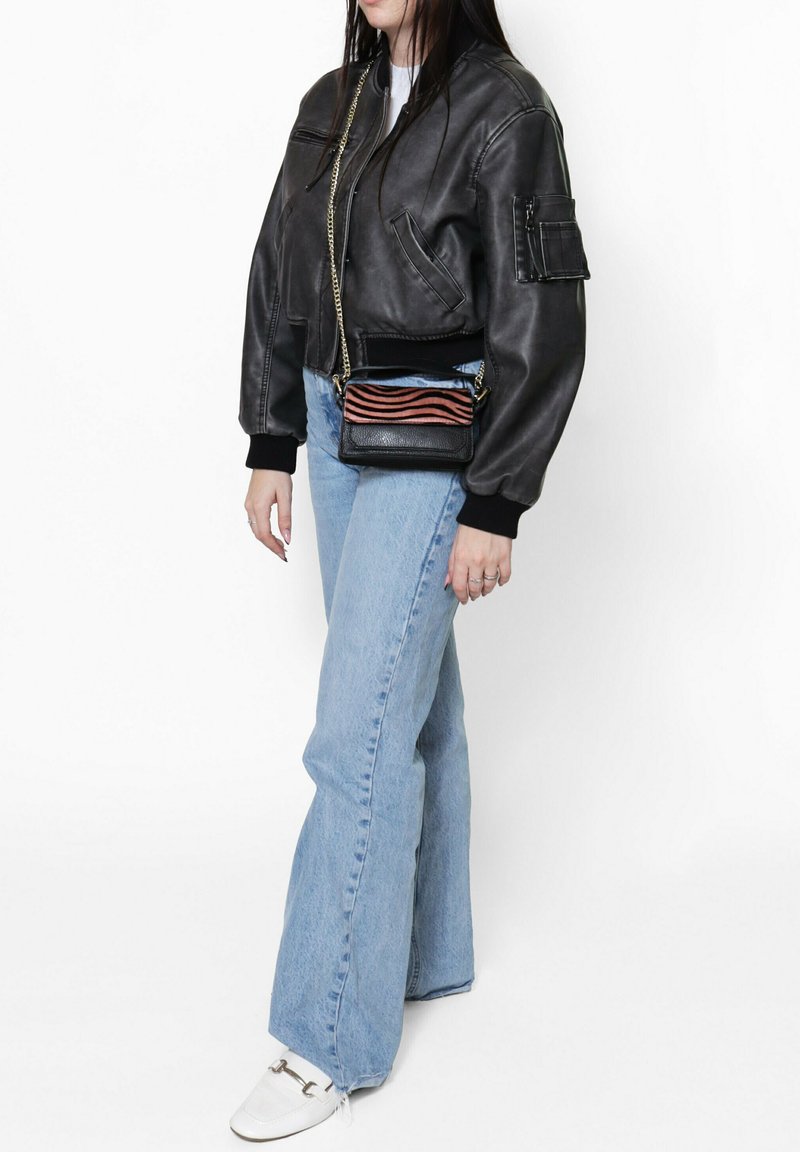 Veste bomber en cuir noir, jeans évasés bleu clair et chaussures blanches avec des éléments en métal argenté. Petit sac noir avec des rayures rouges et bleues.