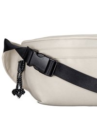 Beige szövet övtáska lapos dizájnnal, fekete állítható pánttal és műanyag csattal. Az oldalán húzózsinóros díszítések találhatók.