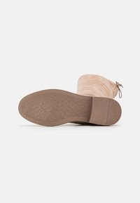 Beige mockasiner som går till knäet, med en texturerad gummisula, rund tå och knytaccent på baksidan. Sulan har ett mönstrat grepp för bra fäste.