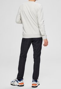 Svetle šedá mikina s kulatým výstřihem, měkká textura. Černé kostkované kalhoty s úzkým střihem, doplněné o vícbarevné tenisky s robustní podrážkou.