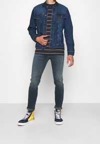 Jeansjacka med två bröstfickor, randig t-shirt, urtvättade blå jeans och högskoor i marinblått med gula detaljer.