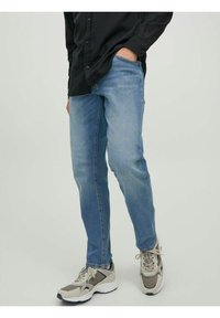 Ljust blå denimjeans med slim fit, synlig söm och framfickor, i kombination med grå och beige sportskor.