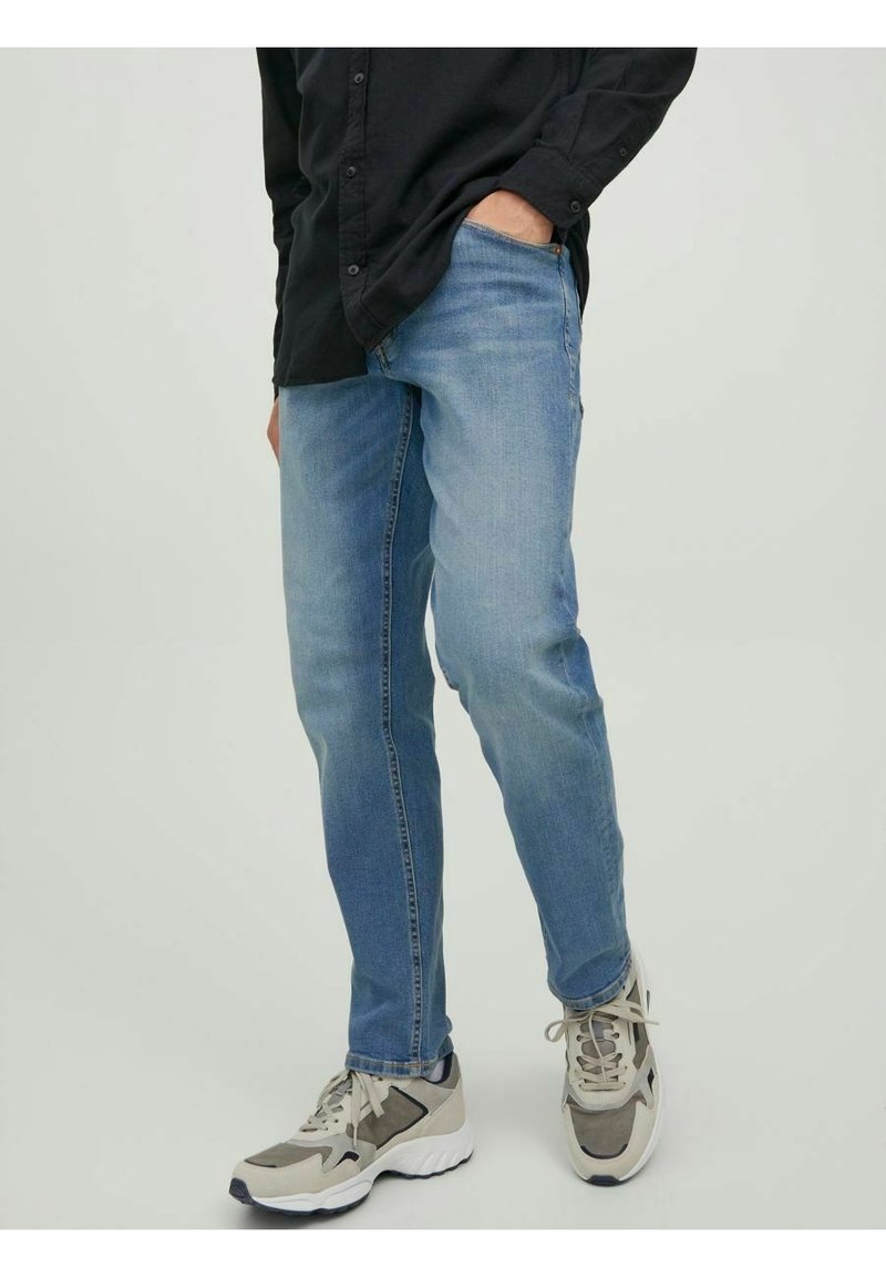 Ljust blå denimjeans med slim fit, synlig söm och framfickor, i kombination med grå och beige sportskor.