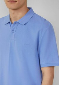 Hellblaues Poloshirt aus strukturiertem Stoff, mit einem Knopfverschluss mit zwei Knöpfen und einem kleinen, eingeprägten Logo auf der Brust. Kurzärmlig.