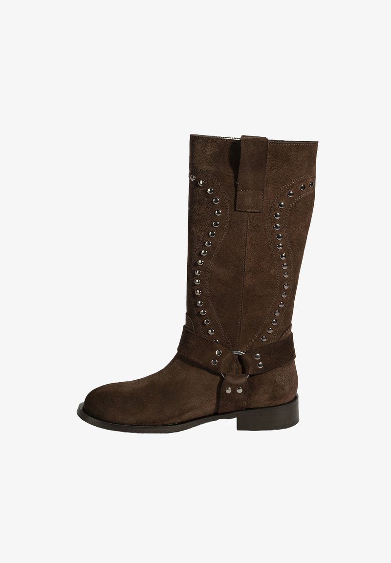 Botte en suede marron hauteur genou avec des accents en clou argentés et un design ceinturé. Elle présente une pointe ronde lisse et un talon bas et plat.