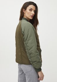 Zelená bomber bunda s rebrovanými manžetami, hladkým povrchom a bočnými vreckami; obsahuje rôzne odtiene olivovej a tmavozelenej.