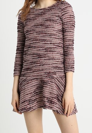 Femme portant une robe en maille texturée dans des tons de violet et de rose avec des manches trois-quarts et un ourlet évasé.