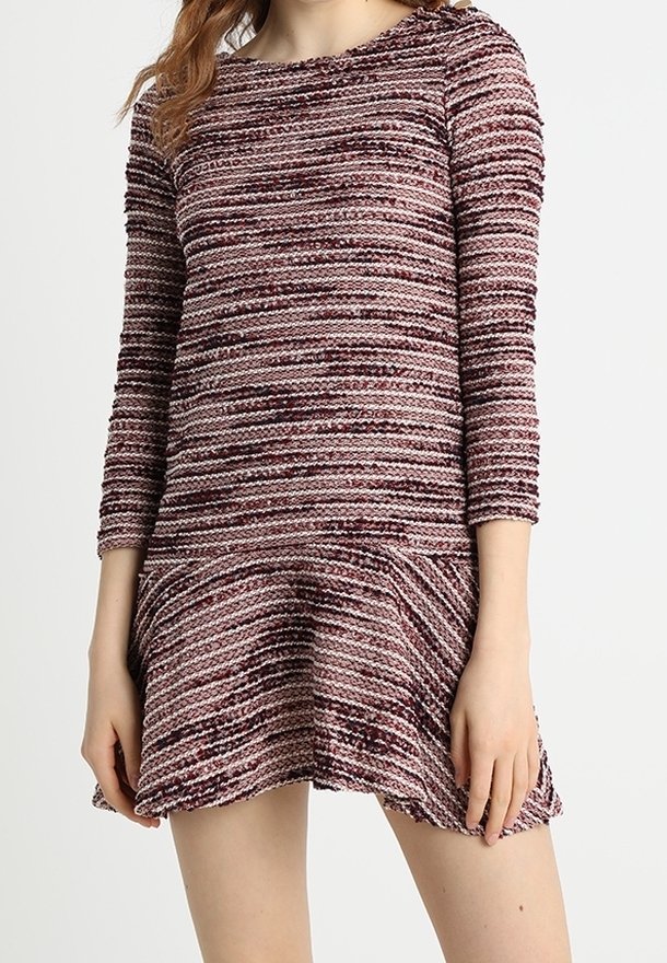Femme portant une robe en maille texturée dans des tons de violet et de rose avec des manches trois-quarts et un ourlet évasé.