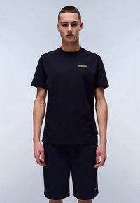 T-shirt nera in cotone con maniche corte, collo rotondo e piccolo logo dorato sul petto. Abbinata a pantaloncini neri in cotone. Design minimalista.