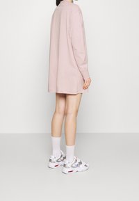 Ljusrosa långärmad klänning, knälång, med rak silhuett. Matchad med vita sneakers med grå och röda detaljer.