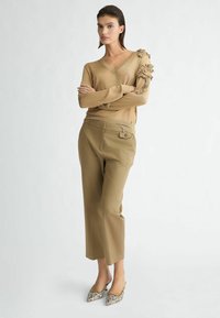 Maglione beige lavorato a maglia con dettagli floreali su una manica, abbinato a pantaloni khaki a vita alta e décolleté con punta a contrasto.