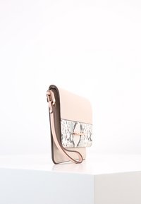 Bolso cruzado con un cuerpo de faux leather rosa claro, acento de impresión de serpiente y una correa delgada. Presenta un cierre magnético y un diseño minimalista.