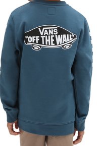 Den blå sweatshirt har en stor svartvita Vans "Off The Wall"-grafik på baksidan, med långa ärmar och ribbade muddar.
