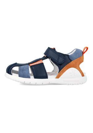 Sandalia en azul marino y azul claro con una combinación de materiales de cuero y ante, diseño de punta abierta, correa ajustable y suela de goma blanca.