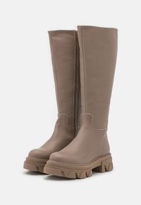 Stivali in pelle beige al ginocchio con finitura testurizzata, zip laterale e suola marrone spessa con un design a bordo ondulato.