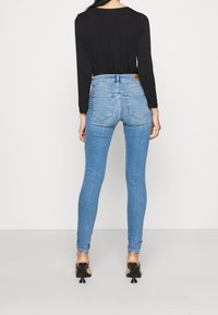 Tajta blå jeans med hög midja, fem fickor och subtil sömnad. Bärs med en svart långärmad topp och svarta klackskor.