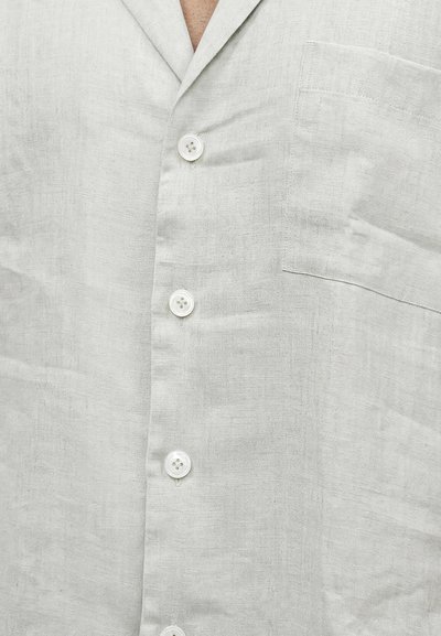 Ανοιχτό γκρι λινό πουκάμισο με τέσσερα λευκά κουμπιά και τσέπη στο στήθος, μερικώς κουμπωμένο με ορατό γιακά και υφή υφάσματος.
