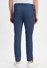 Herren Slim-Fit-Hosen aus strukturiertem blauen Stoff, mit zwei Gesäßtaschen und geradem Schnitt, kombiniert mit weißen Sneakers.