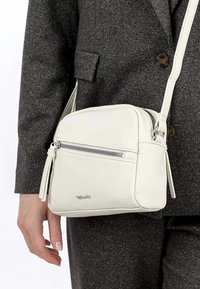 Borsa a tracolla in pelle bianca con forma arrotondata, tasca frontale con zip e finitura texture. Accentuata da una tracolla removibile.