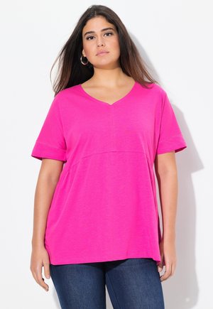 T-shirt rose à col en V avec manches courtes, fabriqué en tissu doux. Présente un design sans couture et une coupe décontractée. Porté avec un jean foncé.