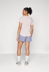 Camisa de manga curta rosa clara com bainha arredondada, combinada com calções lilás. O modelo usa meias brancas e sapatilhas prateadas. Design simples e funcional.