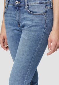 Jeans de mezclilla azul claro con un diseño ajustado, estilo de cinco bolsillos y una sutil textura desgastada. Presenta un botón de metal y cremallera.