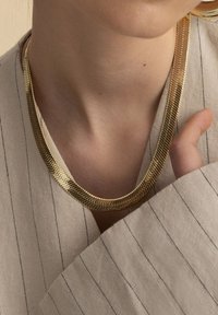 Guldkedja med ett rundat, flexibelt design och en texturerad yta. Buren över ett lätt, randigt tyg.