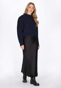 Navyblauer, strukturierten Strickpullover mit langen Ärmeln, kombiniert mit einem schwarzen Satin-Midirock und schwarzen Stiefeletten mit Schnallenakzenten.