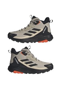 Bottines beiges d'extérieur avec des accents noirs et trois bandes noires. Présentent un dessus texturé, une semelle en caoutchouc et des détails orange vif.