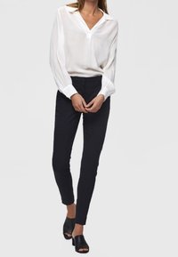 Biała bluzka z długim rękawem, z dekoltem w serek i marszczonymi mankietami; w komplecie z eleganckimi granatowymi spodniami i czarnymi, odkrytymi czółenkami.