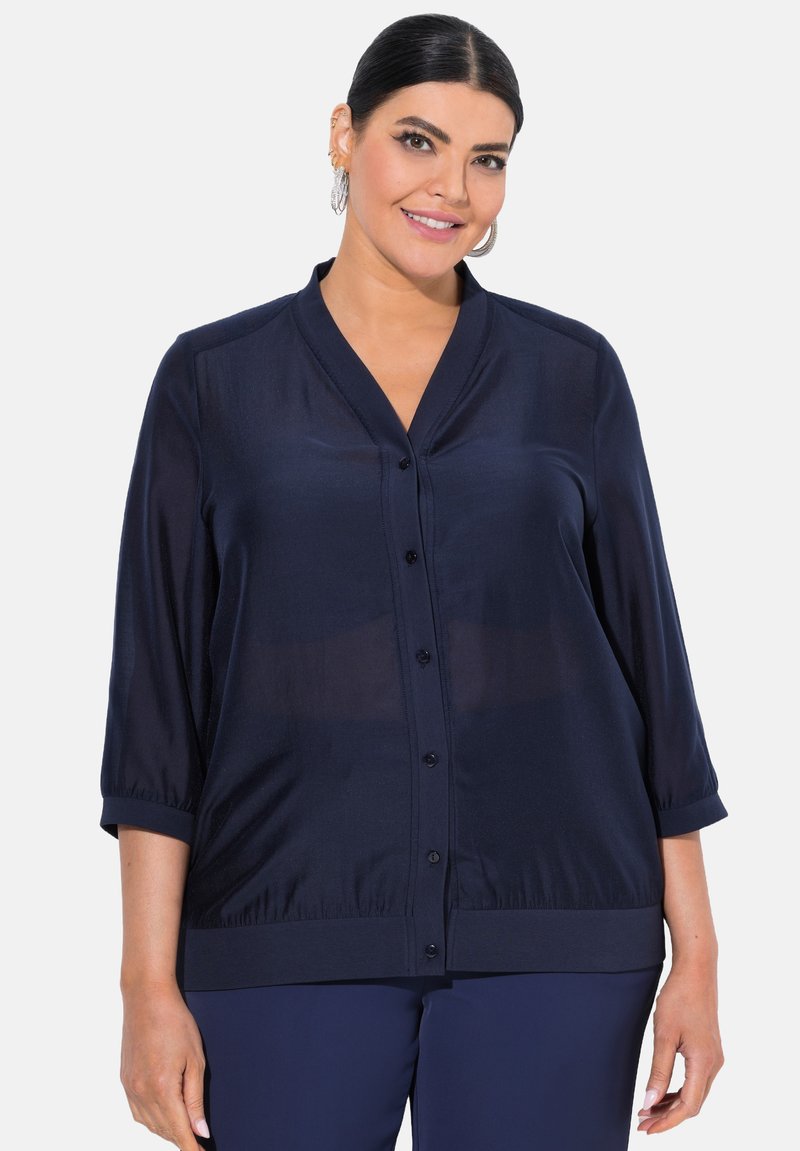 Laivastonsininen napitettava paita, jossa on V-pääntie, kolme neljännestä hihaa ja resorireuna. Tasainen, kevyt kangas, jossa on hieman läpikuultava pinta.