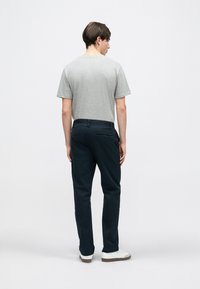 Γκρι κοντομάνικη μπλούζα, μπλε σκούρο παντελόνι με πίσω τσέπες και λευκά αθλητικά παπούτσια. Απλός σχεδιασμός με άνετη εφαρμογή και ομαλή υφή.