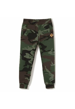 Dziecięce spodnie dresowe w kamuflażowe wzory z elastycznym pasem, kieszeniami po bokach, ściągaczami przy kostkach oraz małą brązową naszywką z logo na prawej kieszeni.