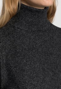 Mörkgrå turtlenecktröja med mjukt, texturerat stickat och åtsittande design, med hög ribbad krage och slät tygoverflá.