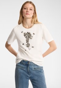 Camiseta de algodón blanca con un diseño floral compuesto por cuentas plateadas y pequeños acentos de abeja. Cuello redondo, mangas cortas y corte relajado.